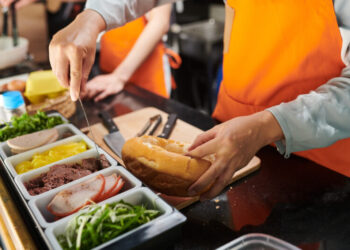 Closeup image of food truck worker putting pork floss in cut wheat bun